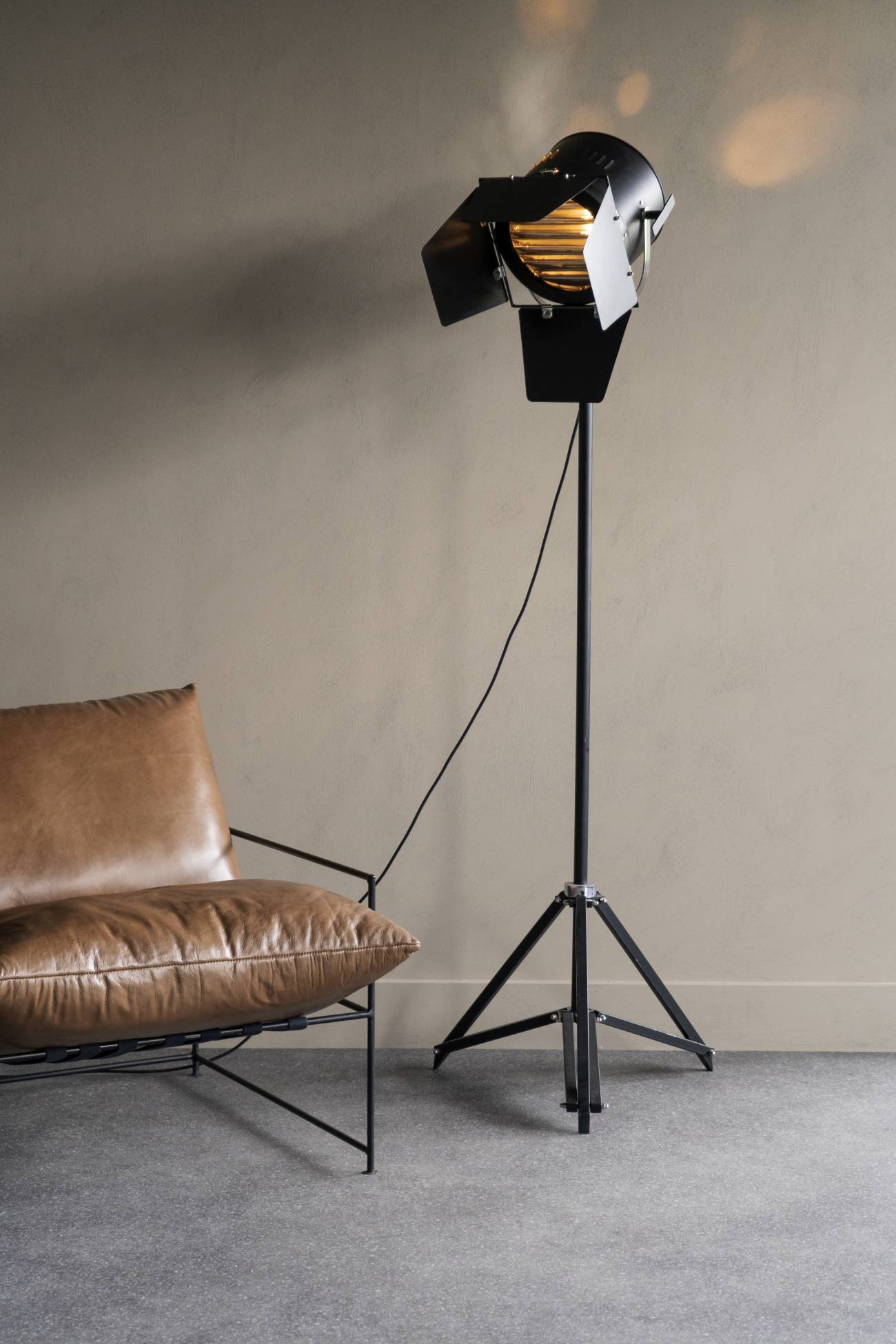 Floor lamp with a vintage design next to a brown leather chair against a beige wall.