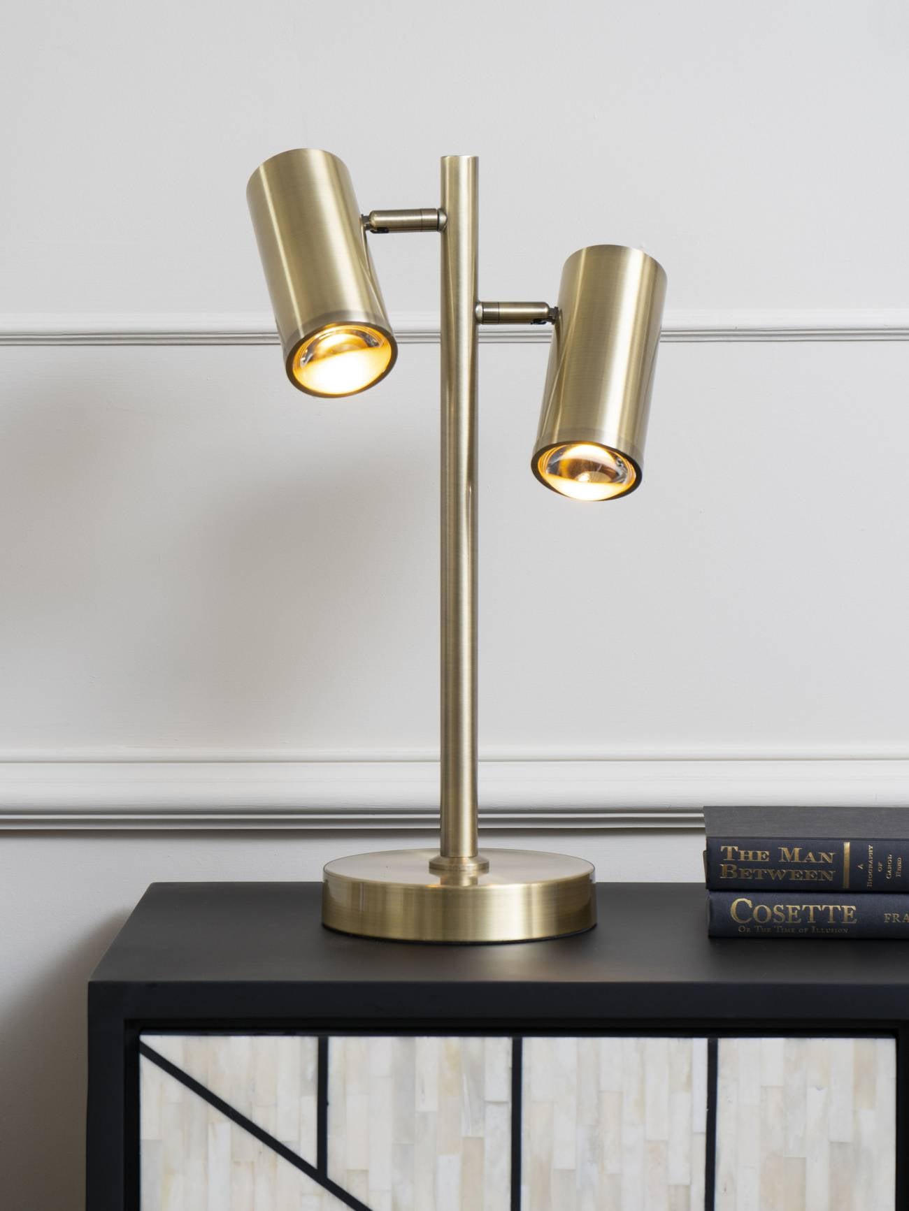 Gold table lamp on a black surface with a white wall background