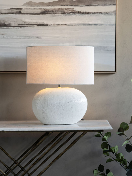 White textured table lamp on a marble surface with abstract art in the background